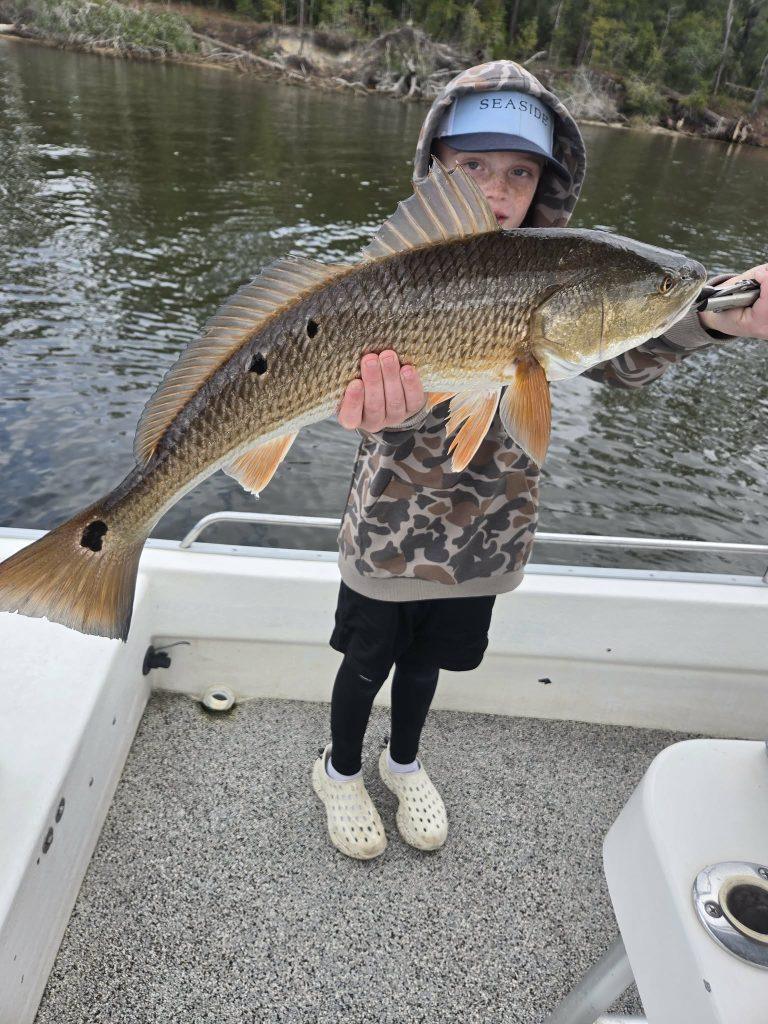 Boy proudly holding redfish caught on kids fishing trip in Choctawhatchee Bay from Santa Rosa Beach 30A